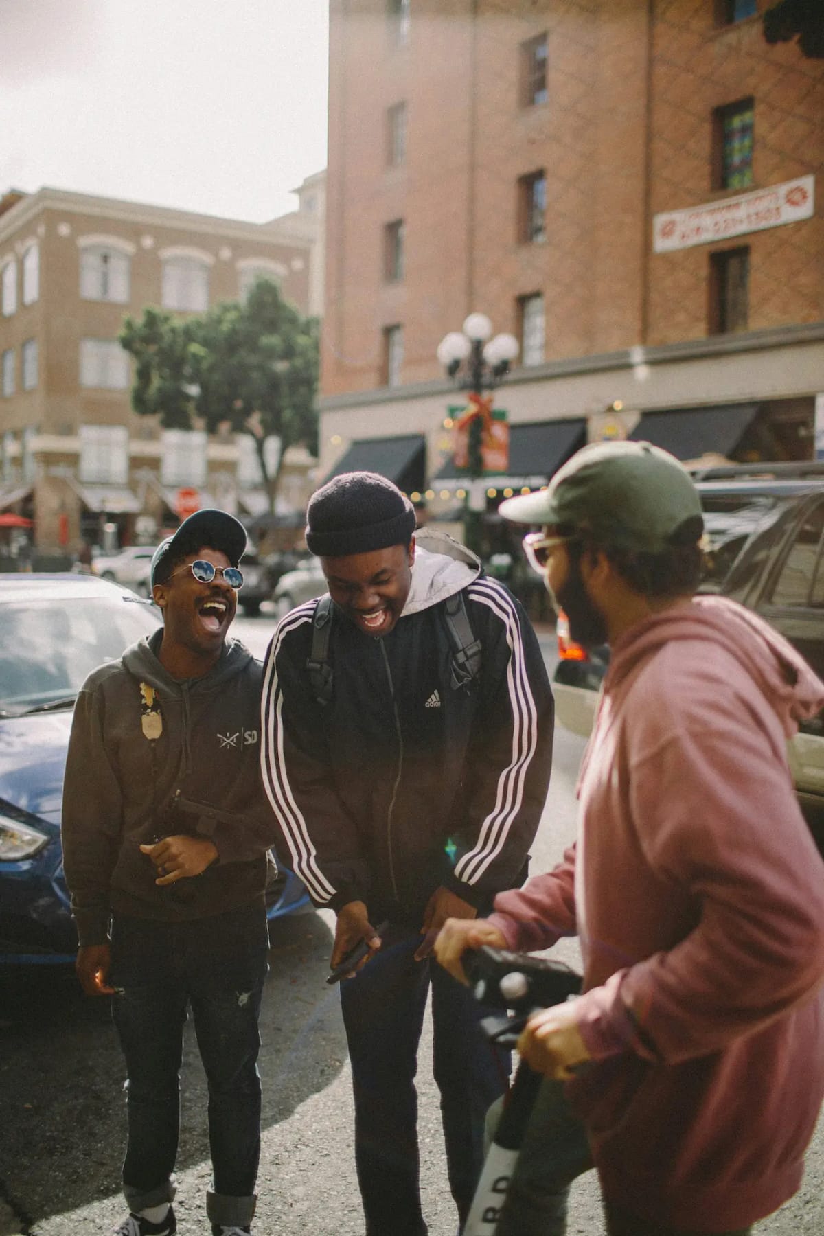 three men standing and laughing in front of cars on a city street
